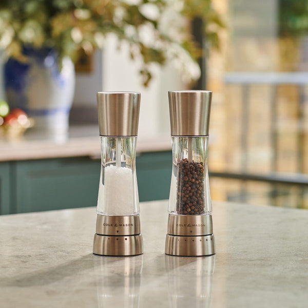 Modern Cole & Mason stainless steel and acrylic  salt and pepper grinders with adjustable grind settings on a kitchen counter