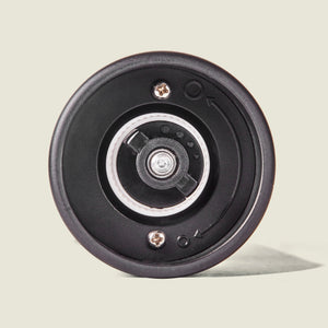 Close-up of the bottom of the Cole & Mason Brixton Electric Mill Matt Black GS, showcasing its ceramic grinder and adjustable grind mechanism with metal screws and embossed directional arrows for grind size adjustment—all thoughtfully designed for easy one-handed operation, set against a plain light background.
