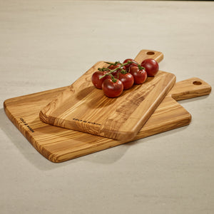 Three Cole & Mason Portobello Olive Wood Serving Boards are stacked on a countertop, topped with vine-ripened tomatoes. Each board has a handle with a hole, ideal for use as an antipasti or cheese board.
