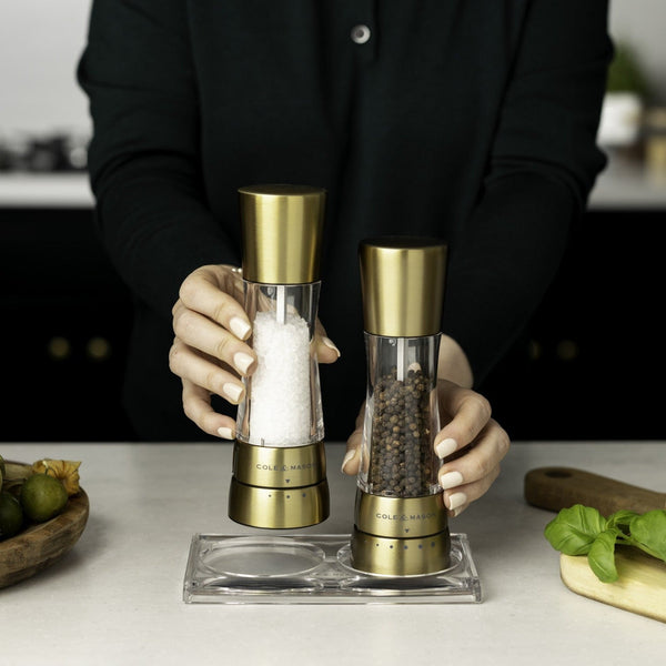 Person using gold salt and pepper shakers on a kitchen counter with food items.