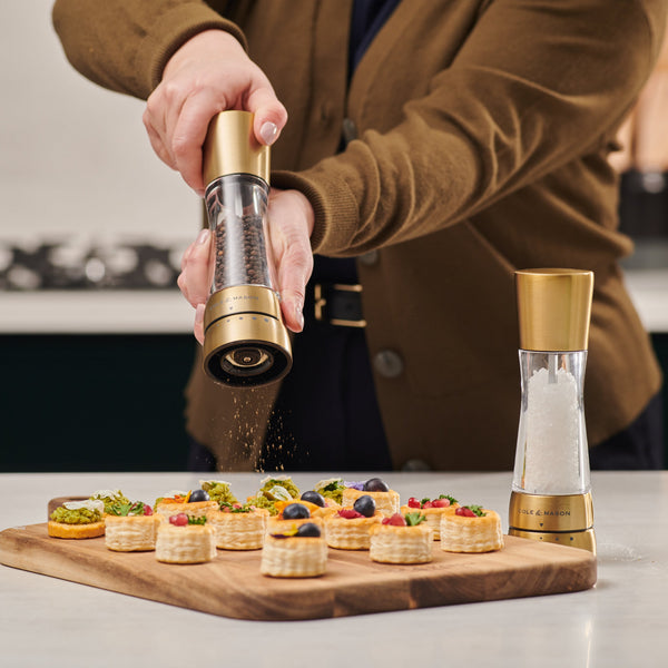 Person seasoning small appetizer plates with a gold and clear salt and pepper shaker.