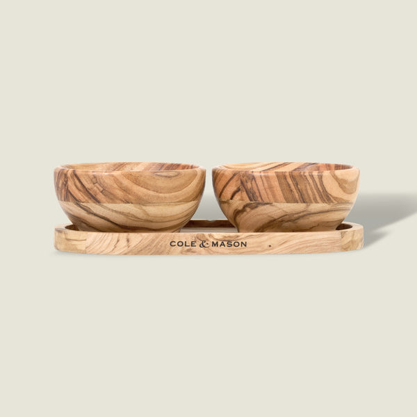 The Cole & Mason Portobello Olive Wood Pinch Pot Set features two small pots with unique grain patterns on a matching tray engraved with the brand name. The set is displayed against a plain, light beige background.