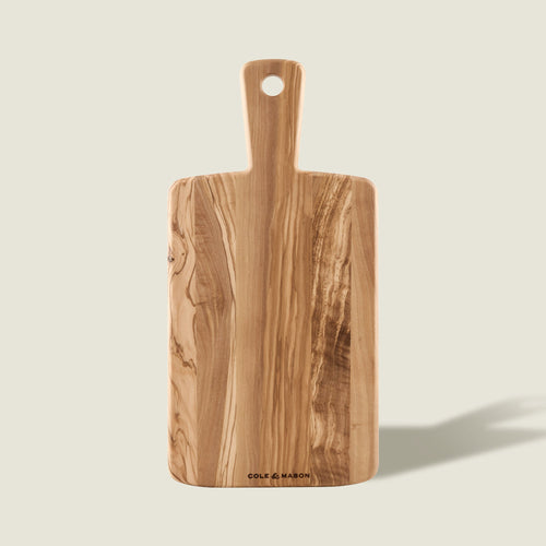 The Cole & Mason Portobello Olive Wood Serving Board is a rectangular Italian board with a handle and rounded edges, showcasing natural grain patterns, a hole in the handle, and the brand name printed at the bottom.