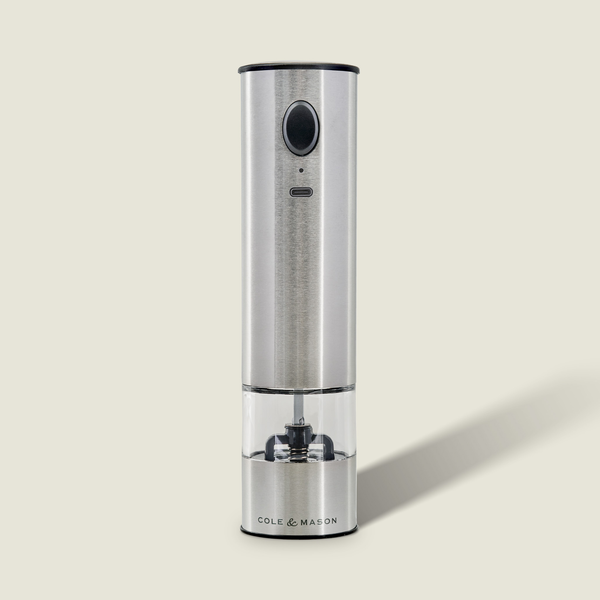 The Cole & Mason Battersea USB Electric Salt & Pepper Mill features a stainless steel design, ceramic grinder, transparent chamber, and front button for one-handed use. It stands upright against a light background.
