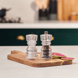 The Cole & Mason London Acrylic Salt Shaker & Pepper Mill Set sits on a wooden cutting board with sliced radish, bringing contemporary style to a modern kitchen.