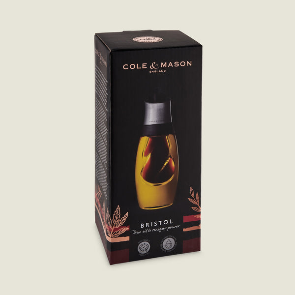 The Cole & Mason Bristol Duo Oil & Vinegar Pourer features a dual-chamber glass design for mess-free dispensing and comes in black and gold packaging with decorative leaf graphics.