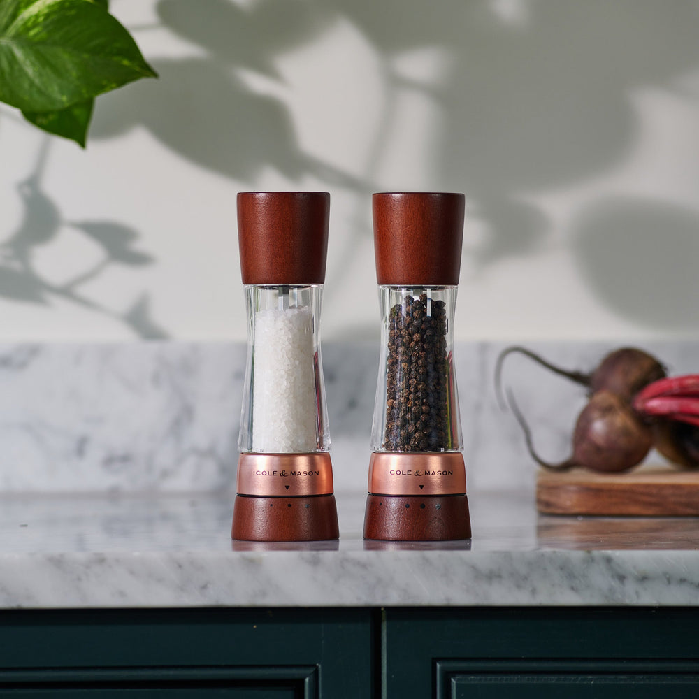 #salt&pepperset
The Cole & Mason Derwent Chestnut Rose Gold Salt & Pepper Mills—featuring clear acrylic bodies, rose gold accents, and chestnut wood tops and bases—stand upright on a light background with salt in one and peppercorns in the other.