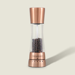 A Cole & Mason Derwent Copper Salt & Pepper Mill, filled with black peppercorns and featuring precision grind technology, stands upright on a light beige background.