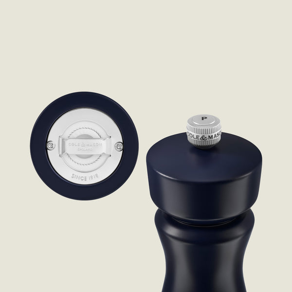 The Kenton Salt & Pepper Mill in Persian Blue Salt by Cole & Mason stands upright next to its detached silver grinding mechanism, with the brand name and “Since 1919” displayed. This stylish mill features a durable ceramic grinder for lasting performance.