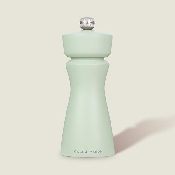 The Cole & Mason Kenton Sage Salt & Pepper Mill features a light green finish, a silver top knob, and a durable ceramic mechanism. It stands upright against a plain, off-white background.