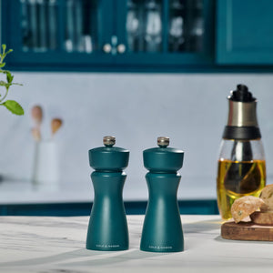 The Cole & Mason Kenton Sea Salt Blue Salt & Pepper Mills, featuring a durable ceramic mechanism, rest on a kitchen counter with blue cabinets and cooking essentials, ideal for contemporary kitchens.