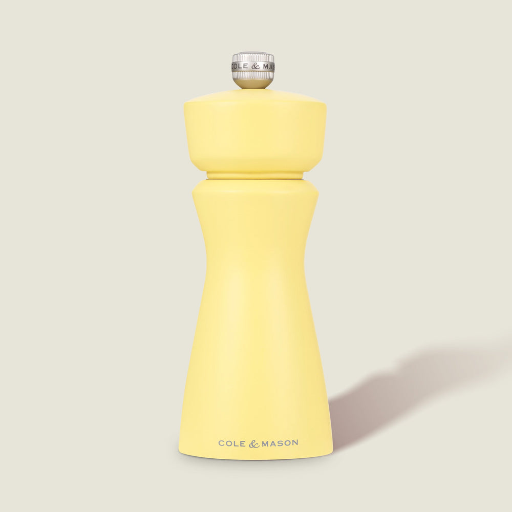 The Cole & Mason Kenton Salt & Pepper Mill in Turmeric Yellow features a silver top knob, brand logo at the base, and a durable ceramic grinding mechanism. Its photographed on a plain light background with a soft shadow to the right.