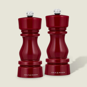 A pair of Cole & Mason London Red Acrylic Salt & Pepper Mills (150mm) stand side by side on a light background, each featuring a glossy red finish, elegant modern curves, silver top knobs, and adjustable grinding mechanisms for customized seasoning.