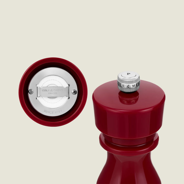 The Cole & Mason London Red Acrylic Salt & Pepper Mills 150mm are displayed, featuring a close-up of their adjustable grinding mechanism and a top knob labeled "P" for pepper. The premium white interior mechanism, engraved with branding, is commonly found in high-quality acrylic salt and pepper mills.