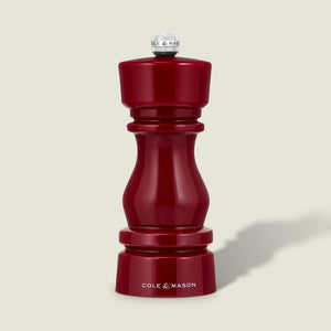 A glossy red pepper grinder from Cole & Mason's London Red Acrylic Salt & Pepper Mills 150mm collection stands upright on a light beige background, featuring a silver knob, the Cole & Mason logo at its base, and an adjustable ceramic grinding mechanism.