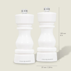 Two Cole & Mason London White Acrylic Salt & Pepper Mills (150mm) stand side by side on a light background. Each features an adjustable grinding mechanism and measures 57mm wide, with measurement lines shown beside the contemporary design.
