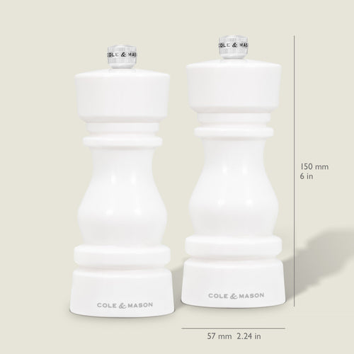 Two Cole & Mason London White Acrylic Salt & Pepper Mills (150mm) stand side by side on a light background. Each features an adjustable grinding mechanism and measures 57mm wide, with measurement lines shown beside the contemporary design.