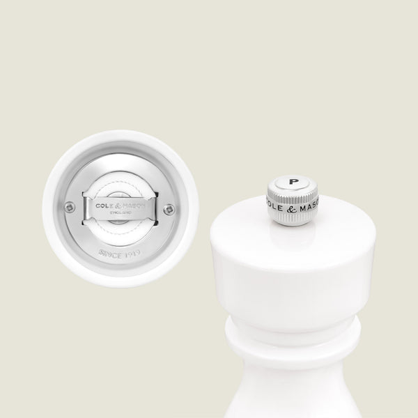 A close-up of the Cole & Mason London White Acrylic Salt & Pepper Mills 150mm highlights the P knob on top and the adjustable grinding mechanism below, set against a plain off-white background.