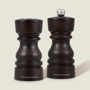 The Cole & Mason London Chocolate Wood Salt Shaker & Pepper Mill Set features two dark wood mills: the pepper mill with grind select technology and a knob, and the shorter, knob-less salt shaker with a premium grinding mechanism.