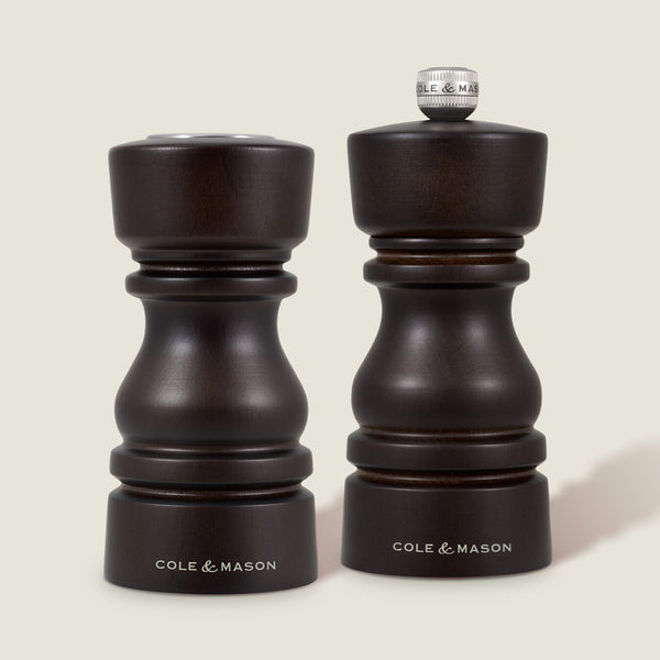 The Cole & Mason London Chocolate Wood Salt Shaker & Pepper Mill Set features two dark wood mills: the pepper mill with grind select technology and a knob, and the shorter, knob-less salt shaker with a premium grinding mechanism.