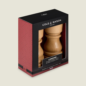 The Cole & Mason London Natural Beech Salt Shaker & Pepper Mill Set comes boxed in black and red packaging with a window, displaying the natural beech mills and featuring product details and branding in white text.