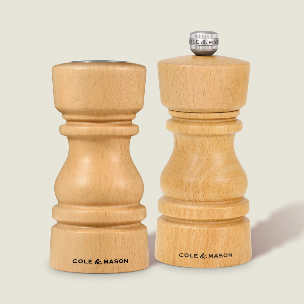 The Cole & Mason London Natural Beech Salt Shaker & Pepper Mill Set, crafted from natural beech wood, stands upright on a light surface. The salt shaker features a silver knob with COLE & MASON engraved, reflecting their elegant design.