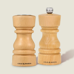 The Cole & Mason London Natural Beech Salt Shaker & Pepper Mill Set, crafted from natural beech wood, stands upright on a light surface. The salt shaker features a silver knob with COLE & MASON engraved, reflecting their elegant design.