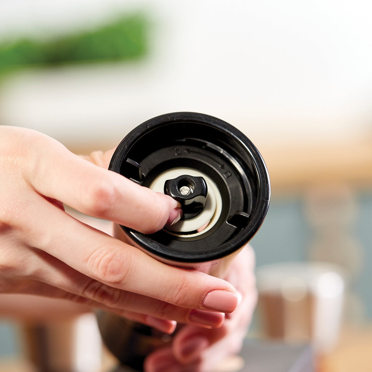 A close-up of a person’s hand adjusting the inner mechanism of a manual coffee grinder, focusing on the grinder’s burr setting.