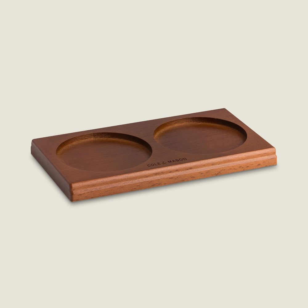 The Cole & Mason Wood Mill Tray is a rectangular wooden tray with two round indentations for holding salt and pepper mills, featuring the engraved brand name on the front edge. Displayed against a light, neutral background.